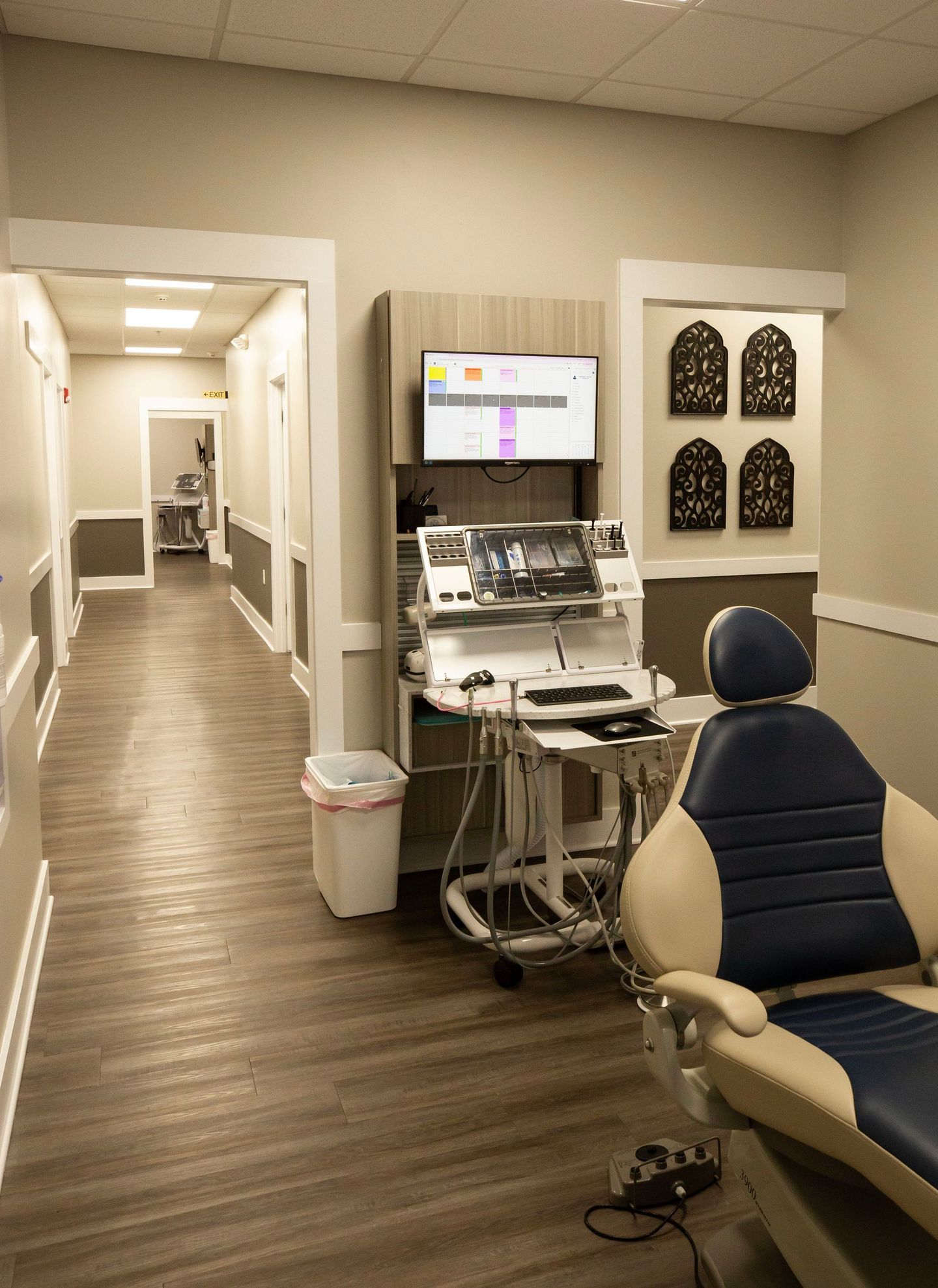 Medical clinic hallway with a workstation, monitor, chair, and exam chair in the foreground