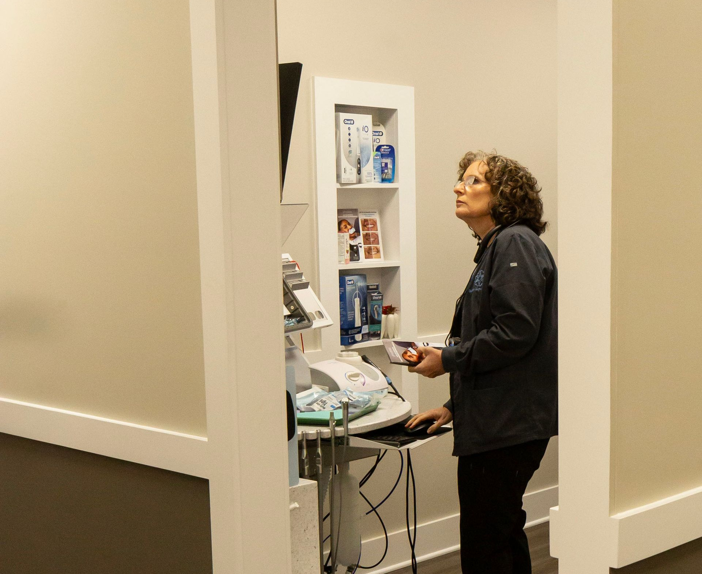 Woman stands at a small table in a beige office hallway beside a wall cabinet and cables.