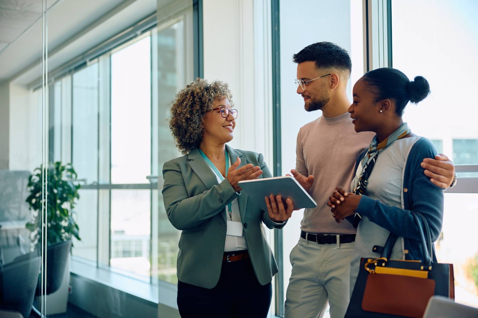 Three coworkers discussing a tablet in a bright office hallway