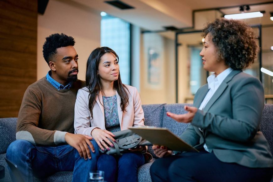 Three people in a meeting, with one speaking and holding a folder in a modern office lounge