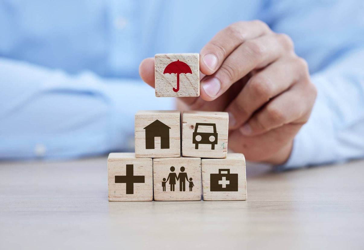 Hand placing a red umbrella block atop stacked healthcare icons on wooden cubes