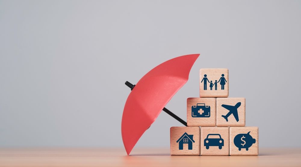 Red umbrella shielding stacked wooden blocks with insurance icons on a table