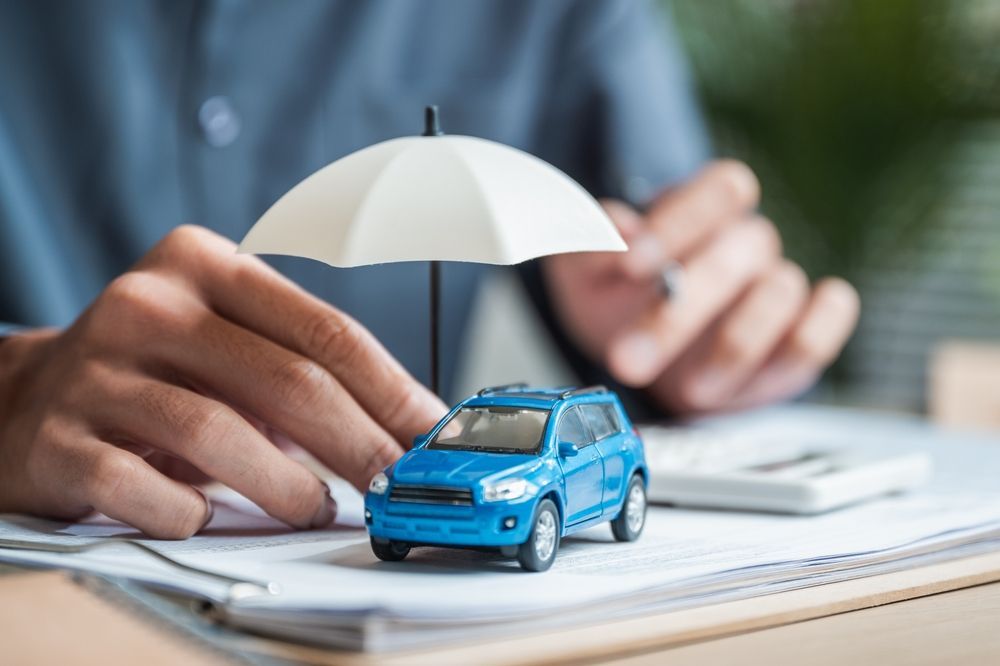 Blue toy car under a small umbrella on a desk with hands in the background