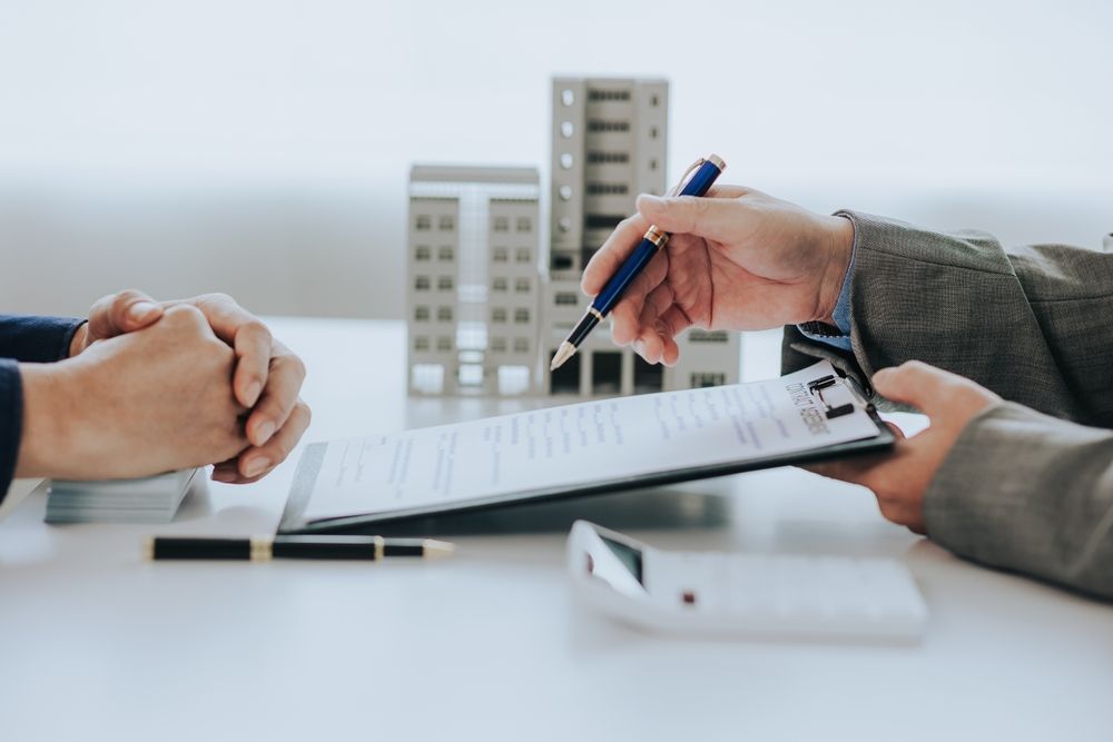 Two people signing a document at a table with a pen and small building models in the background
