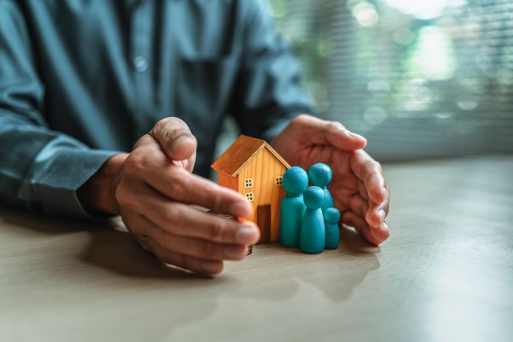 Hands cupping a small house and family figurines on a table