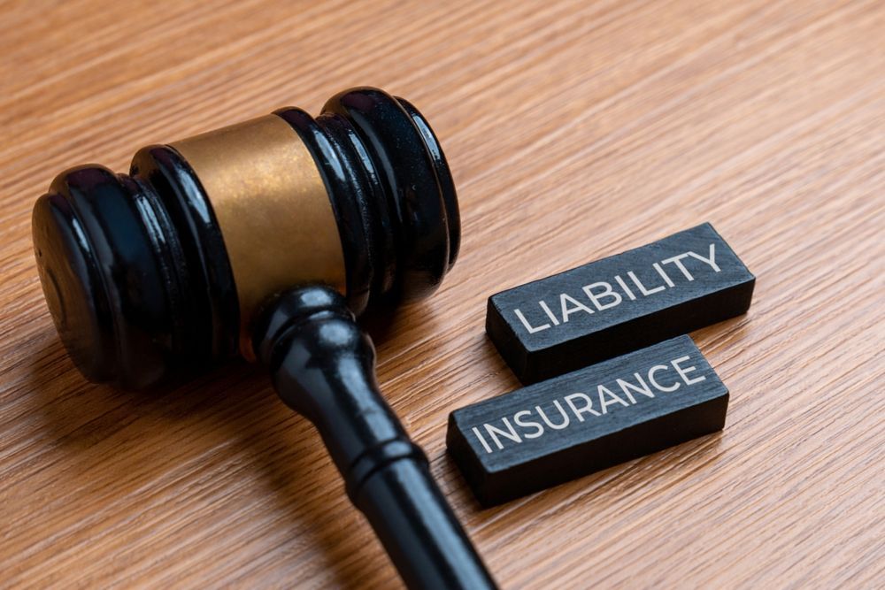 Gavel beside blocks labeled “LIABILITY” and “INSURANCE” on a wooden table.