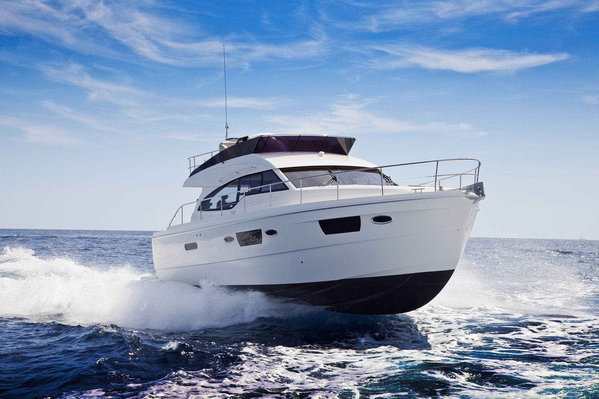 White yacht speeding across open water under a blue sky, leaving a foamy wake