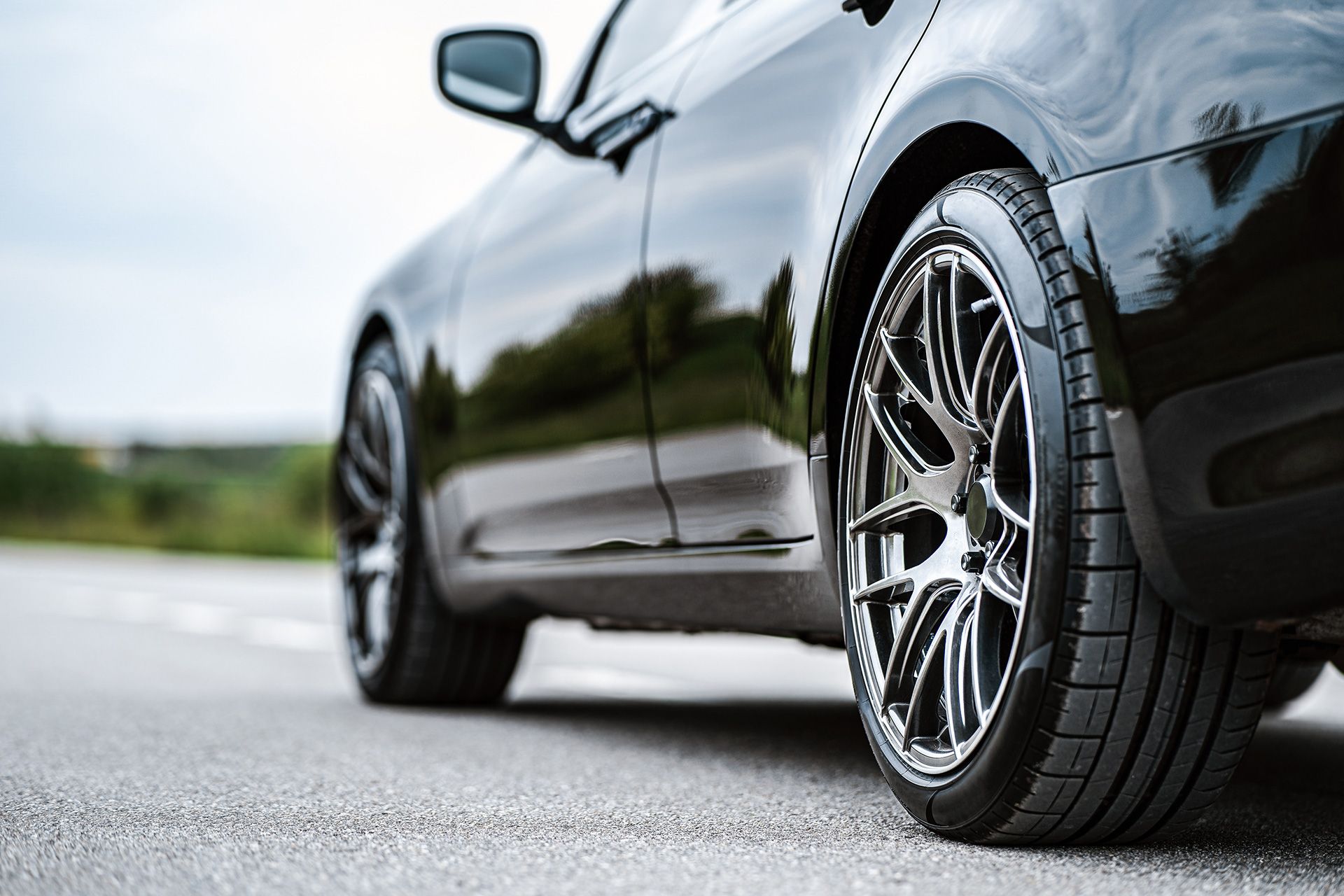 Black sports car parked on a road, close-up of shiny alloy wheels and side body