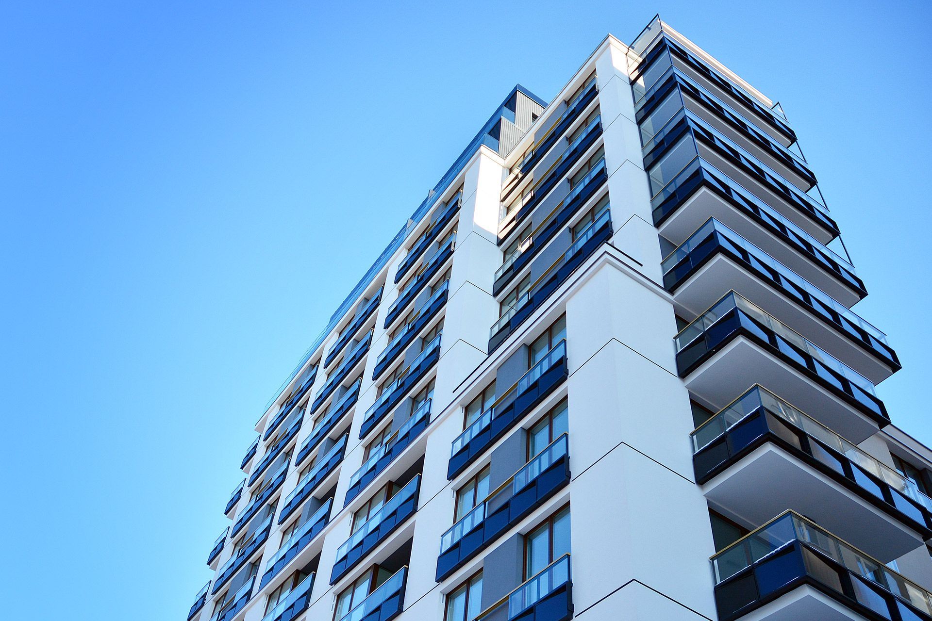 Low-angle view of a modern high-rise building with white and blue balconies against a clear blue sky
