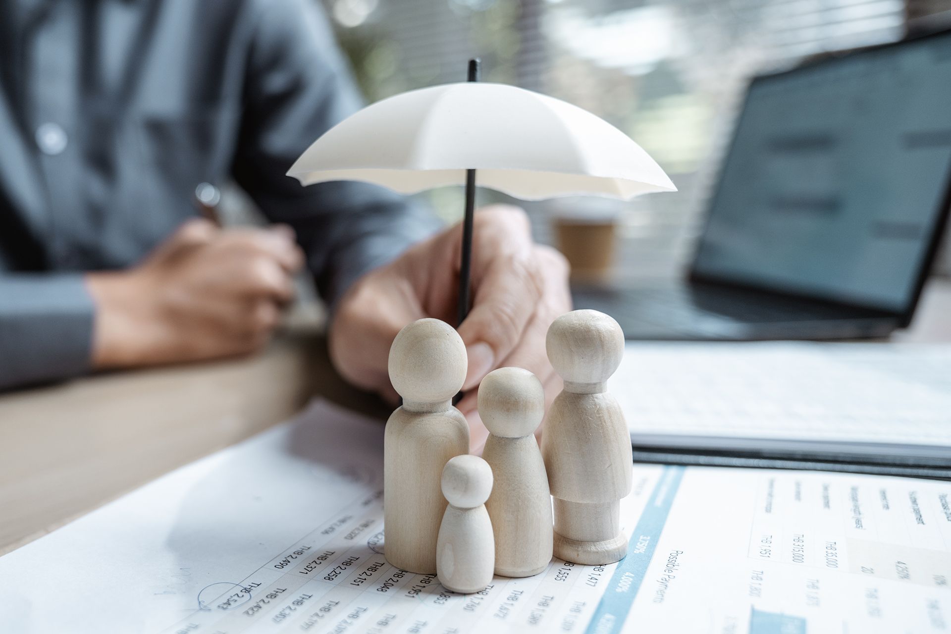 Toy family figures under a white umbrella on insurance paperwork, with a person working in the background