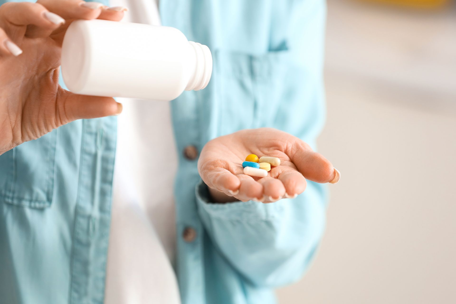 Person holding a pill bottle and colorful tablets in a hand, wearing a light blue medical coat