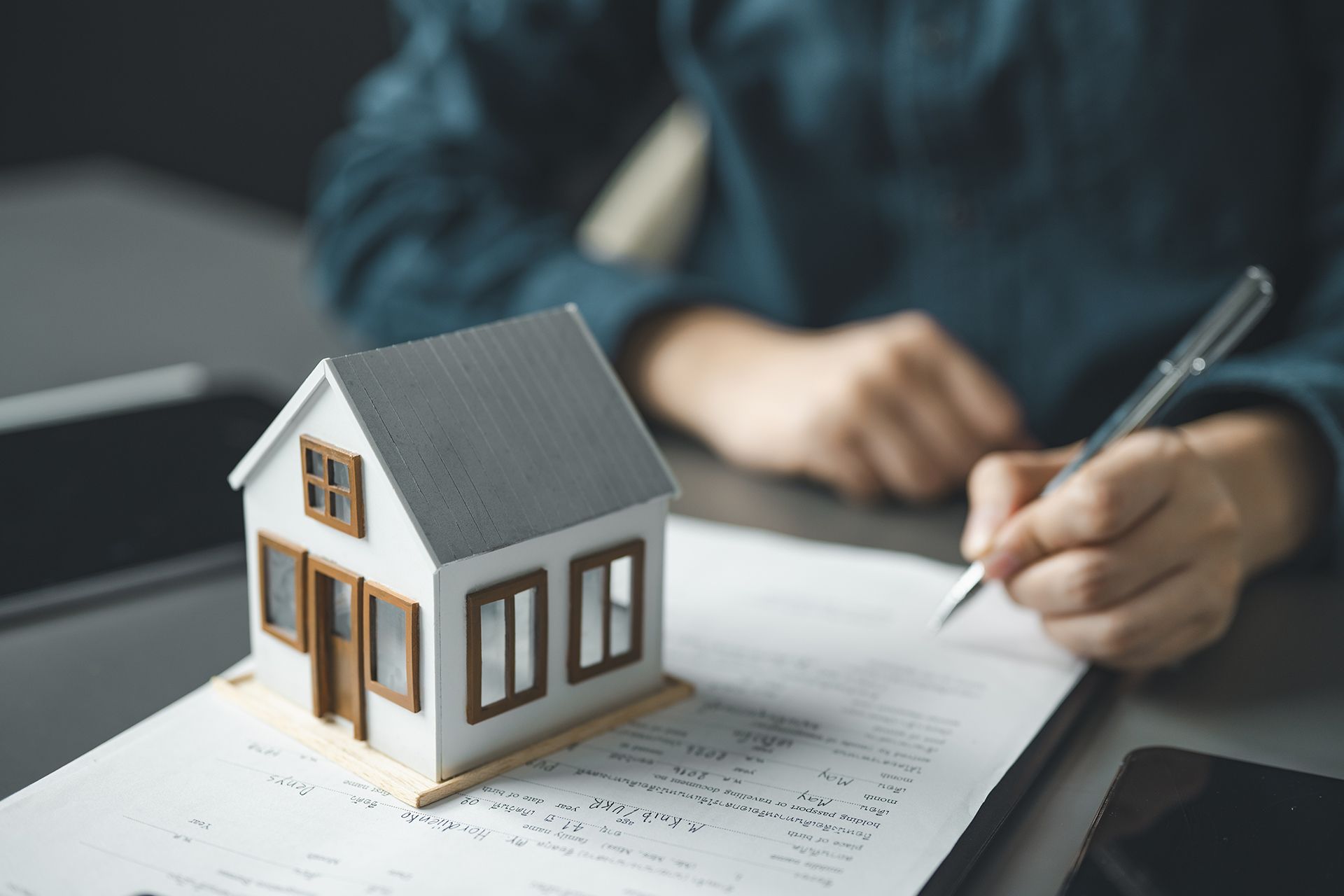 Small house model on paperwork as a person in a blue shirt writes nearby
