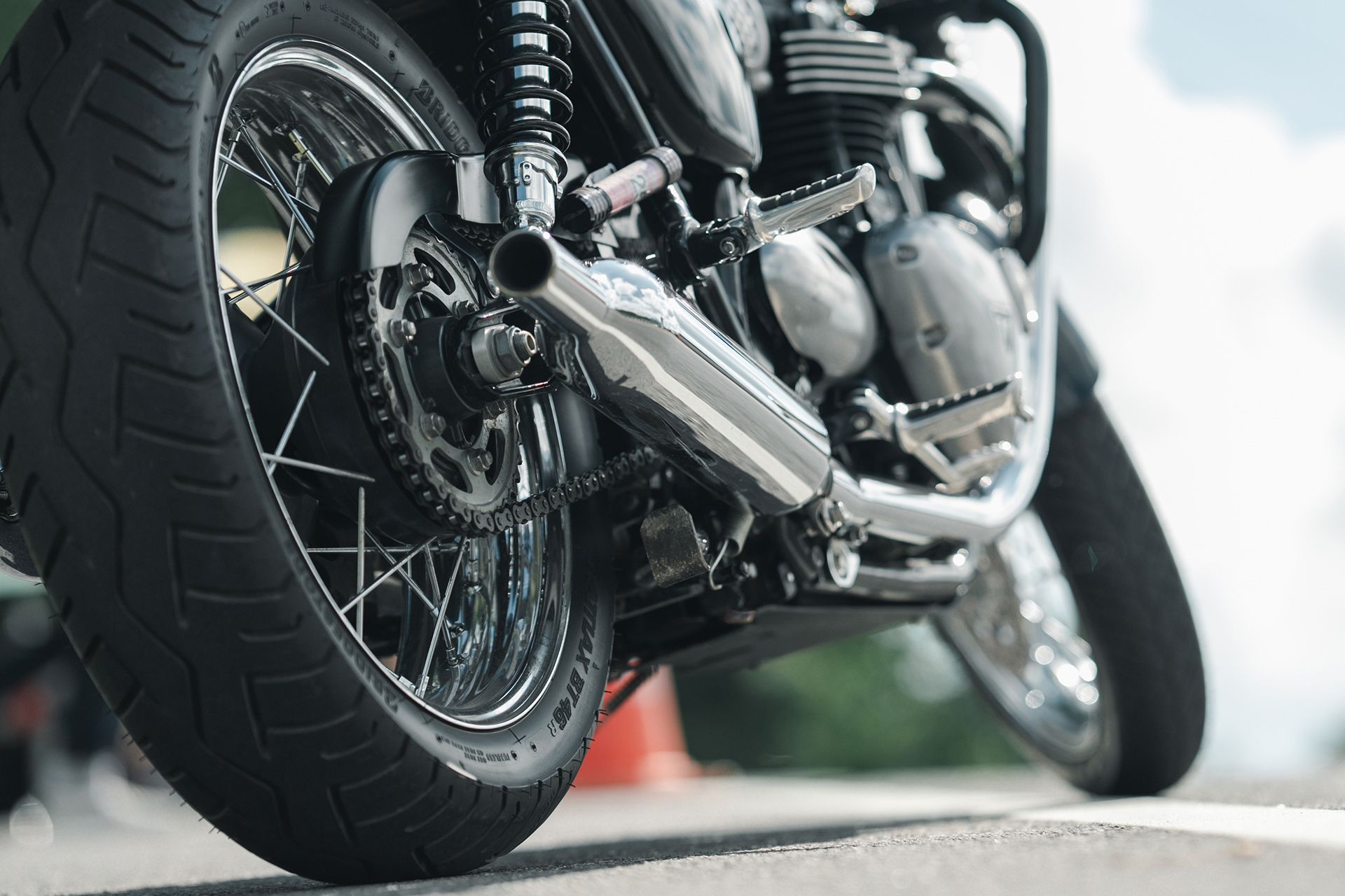 Low-angle view of a black motorcycle’s rear wheel and chrome exhaust on a road.