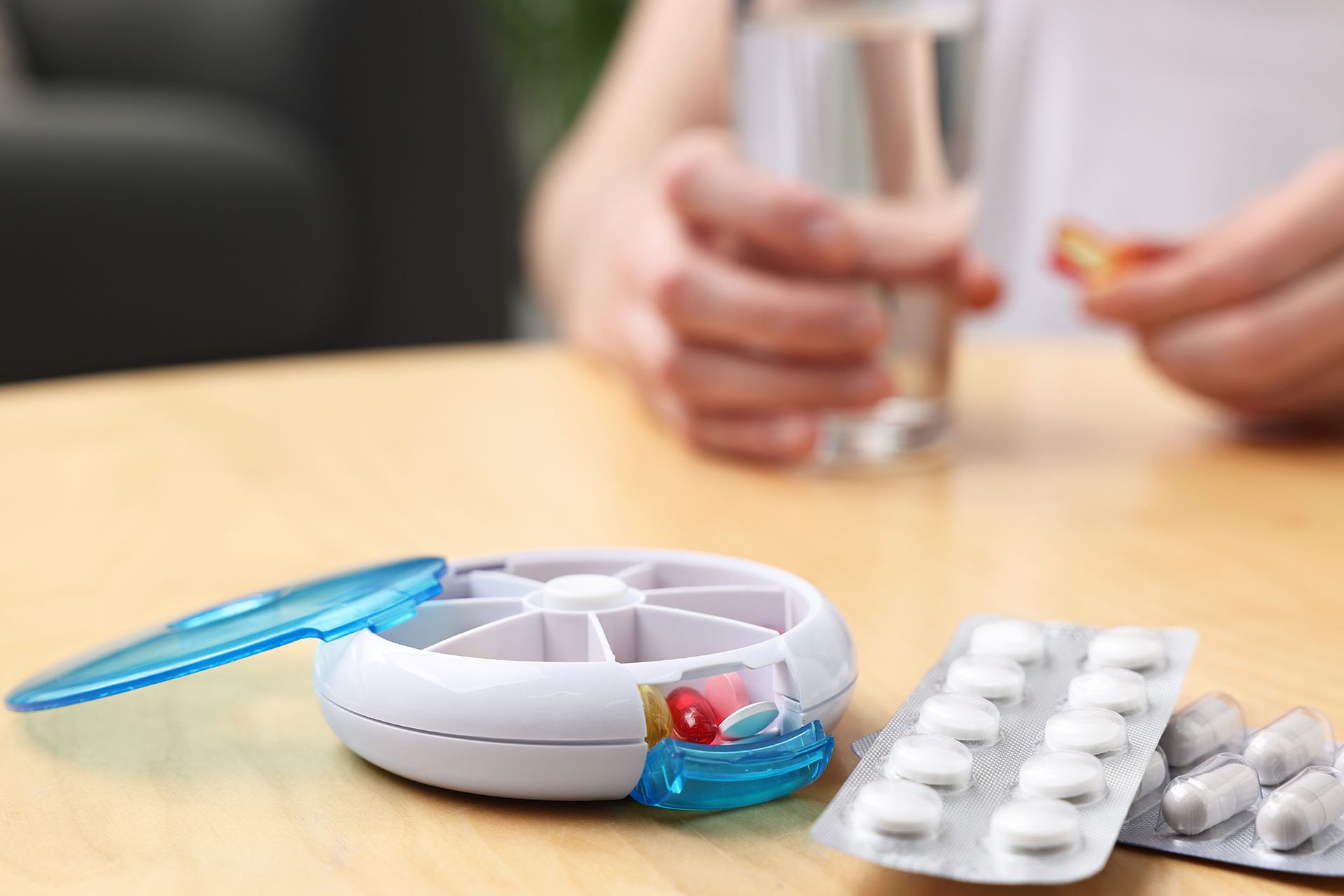 Person opening a pill organizer beside blister packs and a glass of water