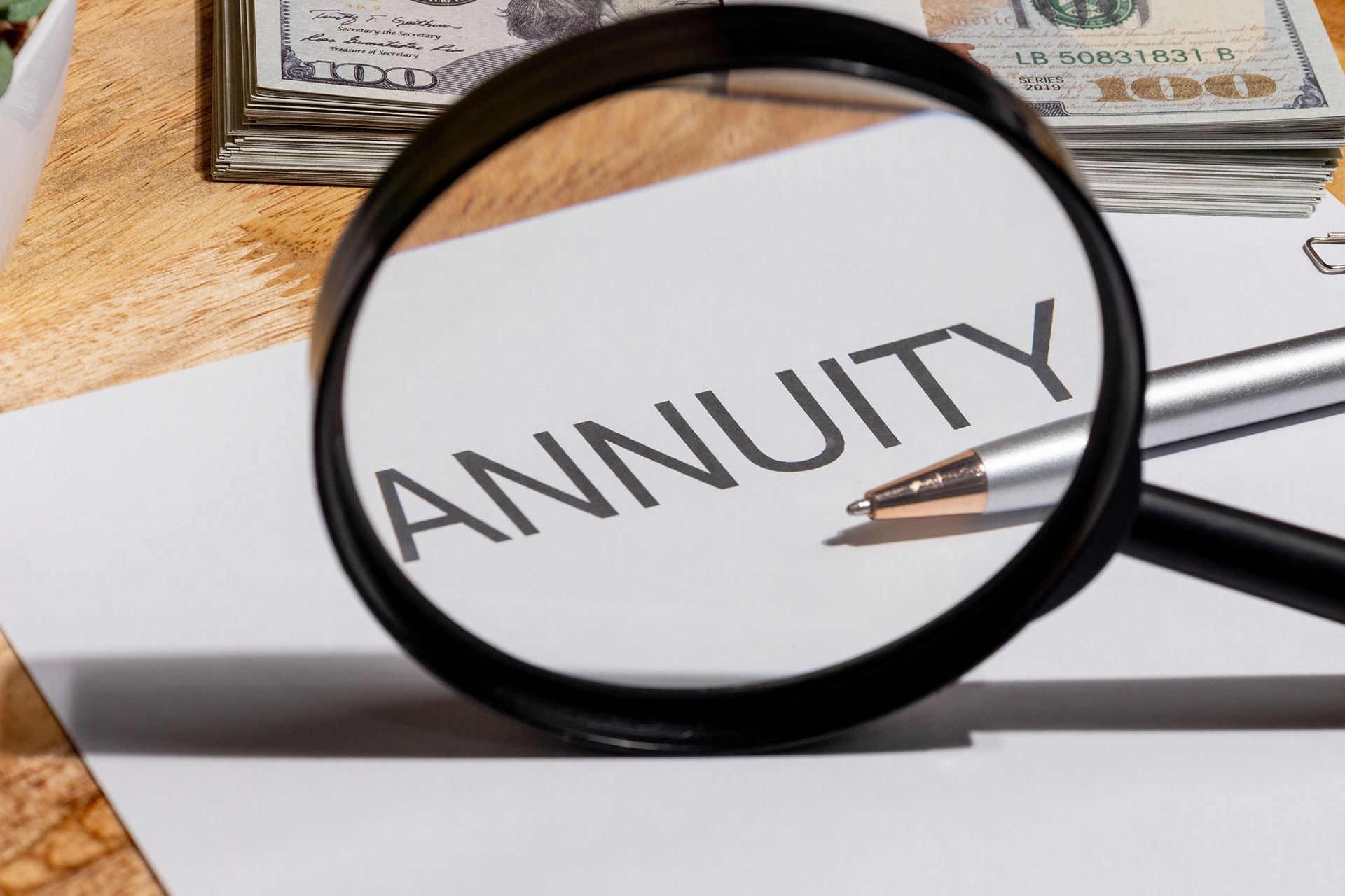 Magnifying glass over the word “ANNUITY” on a document with cash in the background