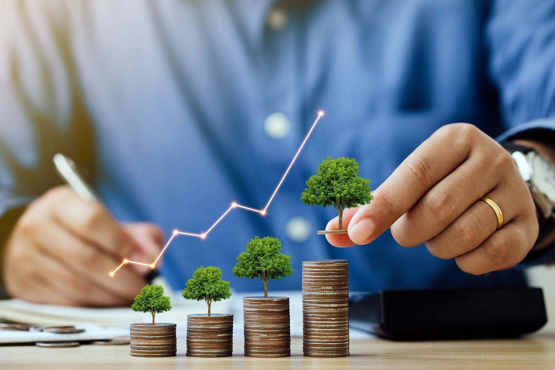 Hands arranging stacked coins with growing plants and a rising line graph on a desk
