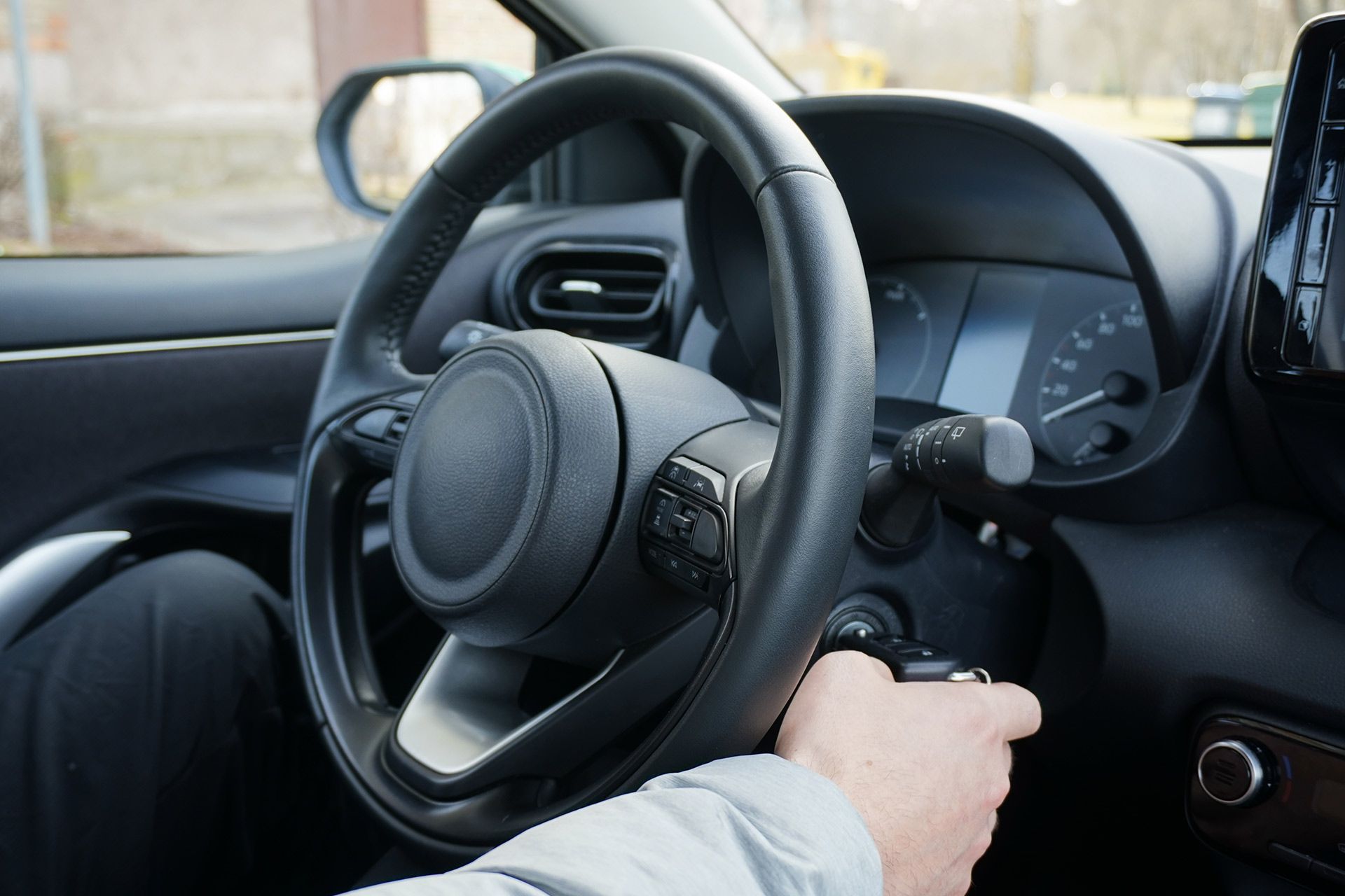 Close-up of a hand turning a car ignition beside the steering wheel and dashboard