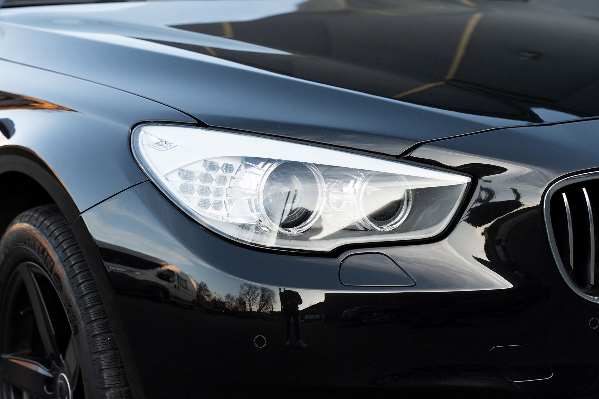 Close-up of a black car’s front headlight and grille on a glossy exterior