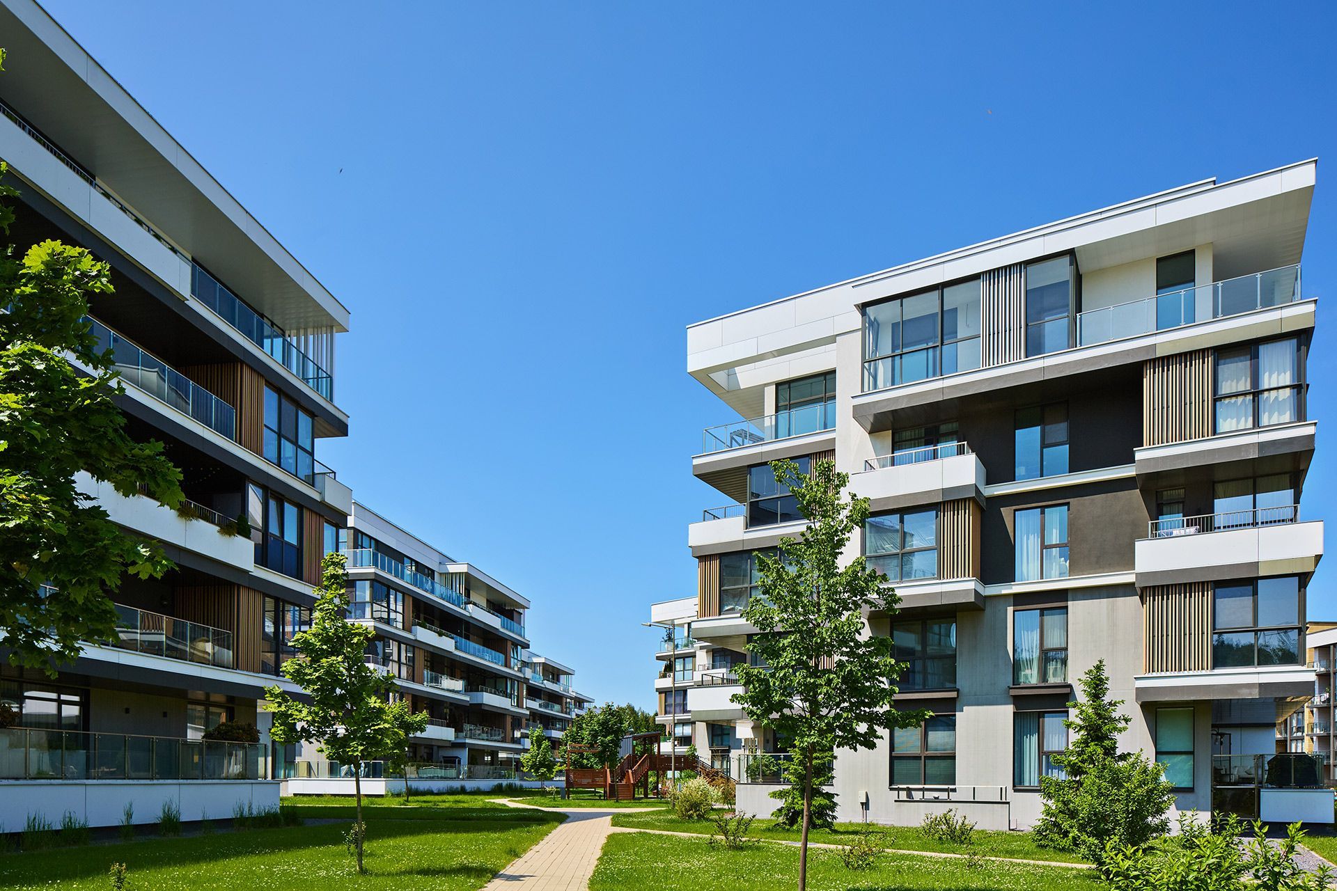 Modern apartment buildings with balconies and landscaped green courtyard under a blue sky