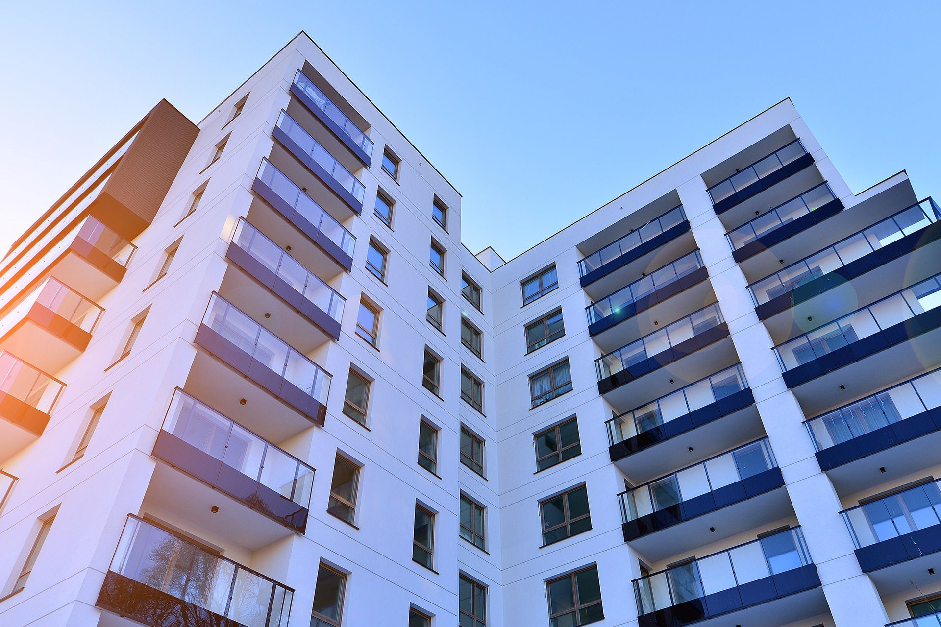 Modern white apartment buildings with blue balconies viewed from below against a bright sky