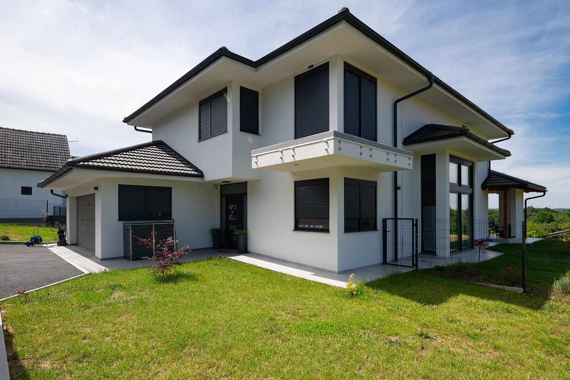 Modern white two-story house with dark trim, a garage, and a green lawn on a sunny day
