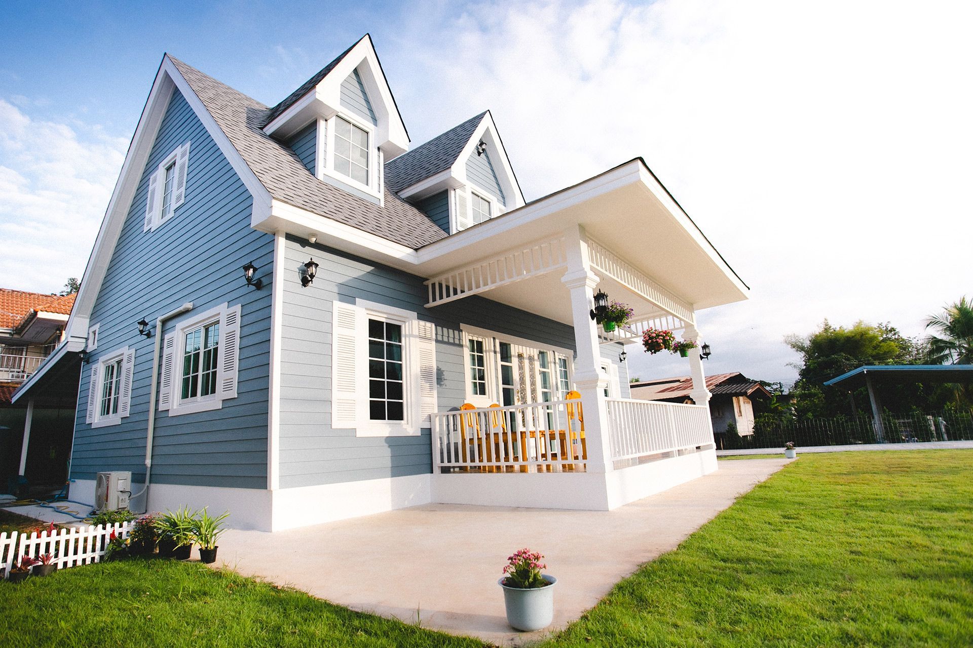 Blue house with white trim, gabled roof, and covered porch on a sunny lawn