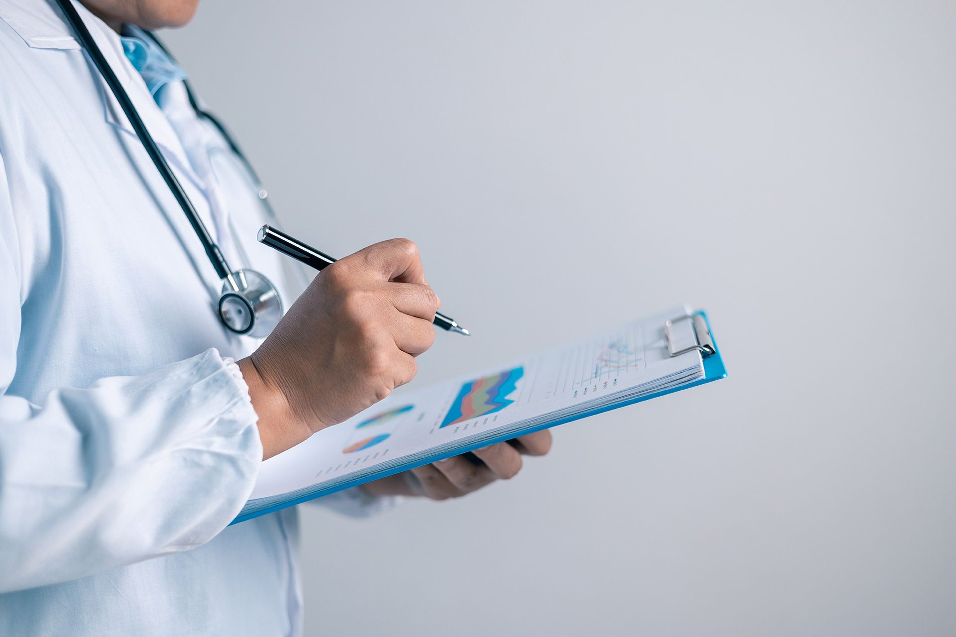Doctor in white coat writing on a clipboard with charts and graphs visible