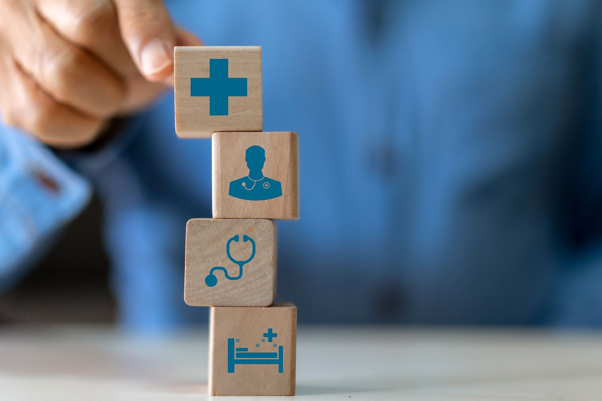 Hand placing stacked wooden blocks with blue medical icons on a table