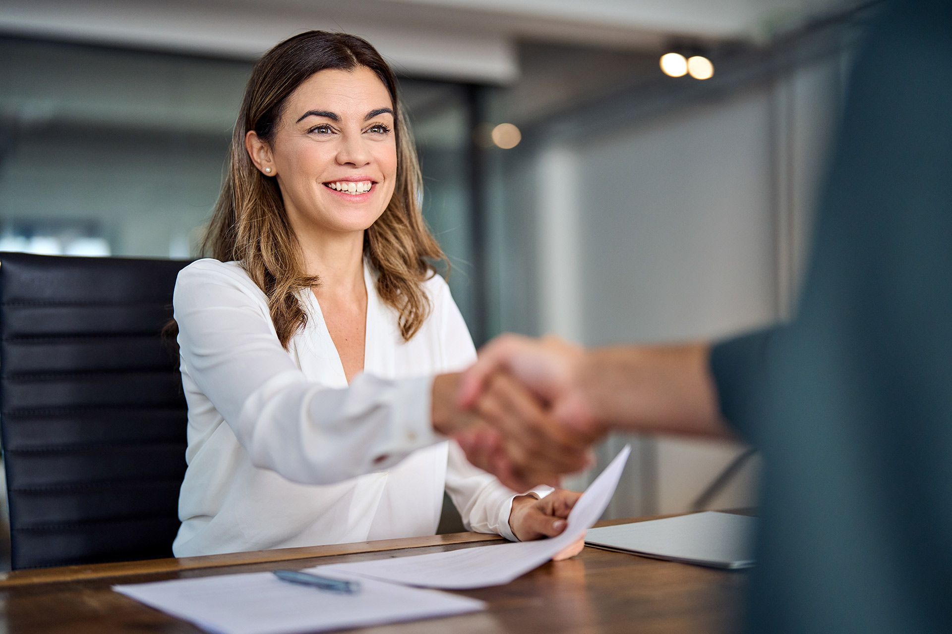 Smiling office worker shaking hands across a desk in a modern conference room