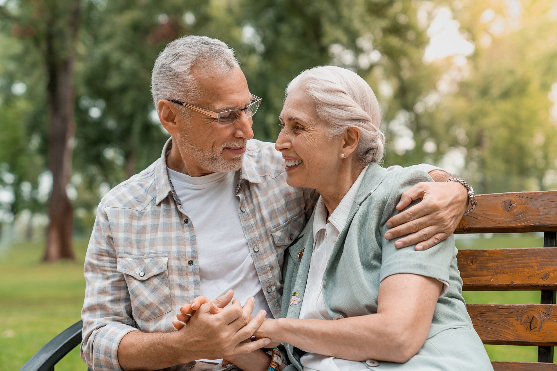 Two elderly people smiling and holding hands on a park bench