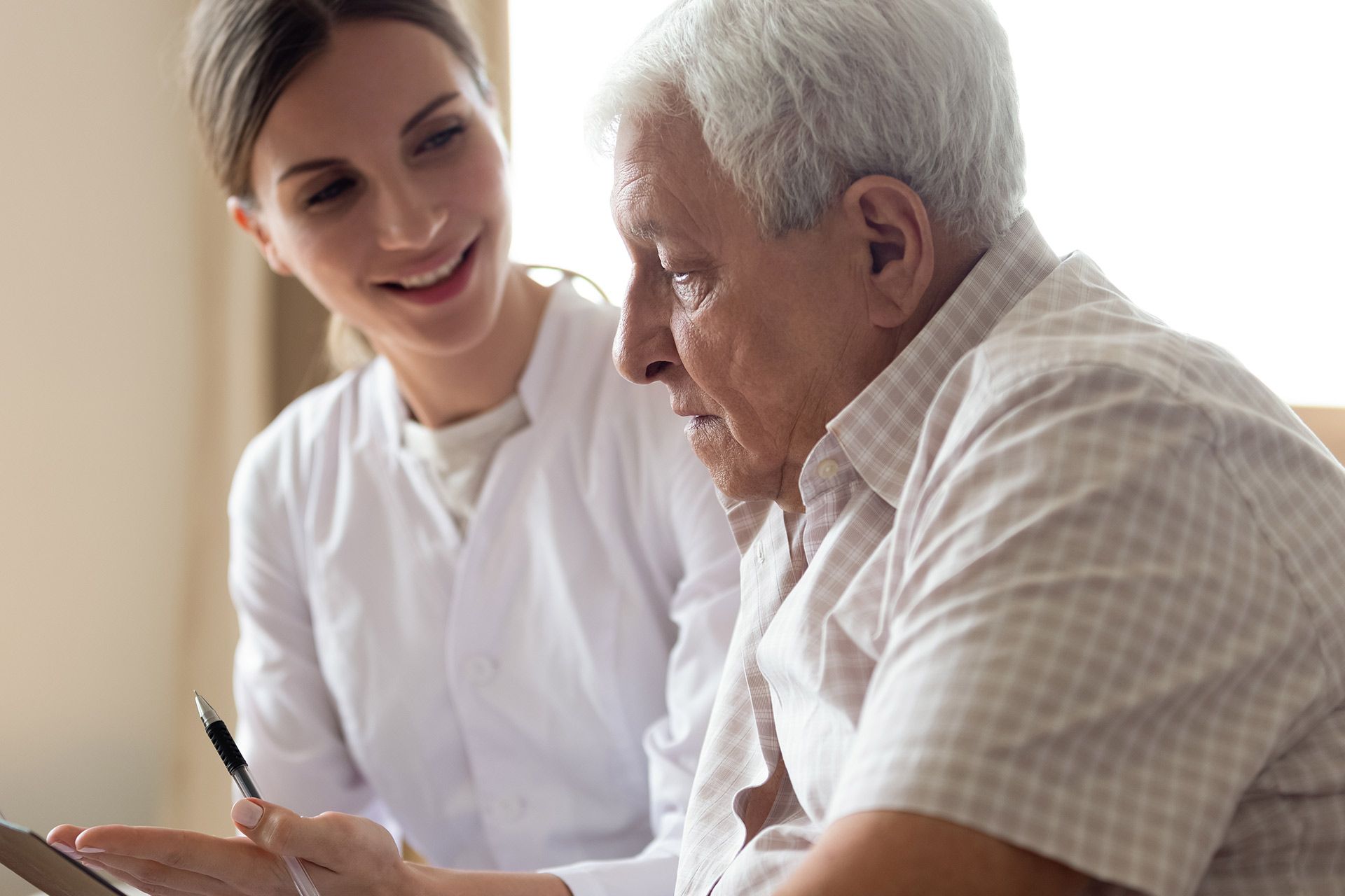 Caregiver showing an elderly man something on a tablet in a bright indoor setting