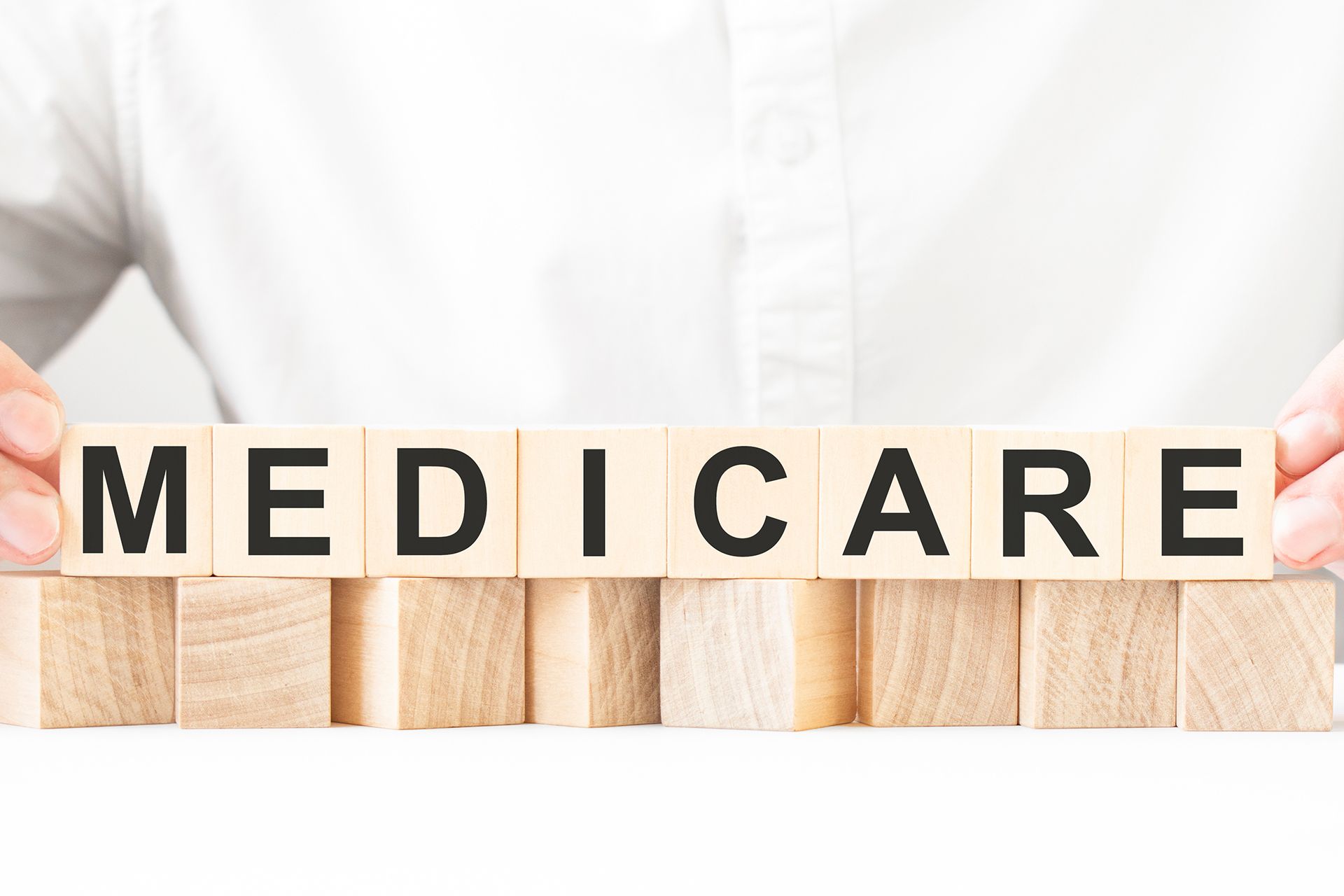Wooden blocks spelling “MEDICARE” held in front of a white shirt