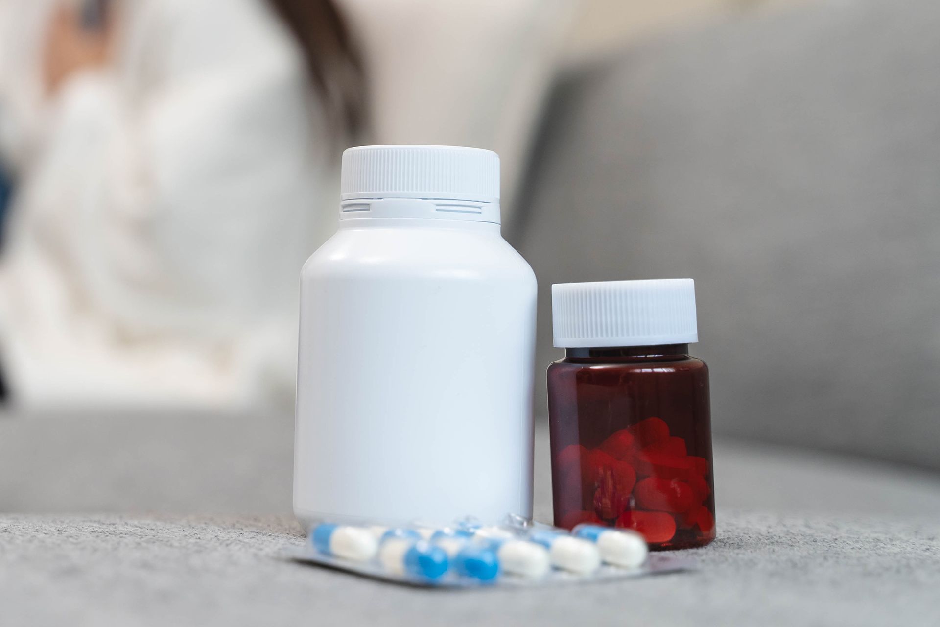 White pill bottle, red liquid medicine bottle, and capsules on a countertop