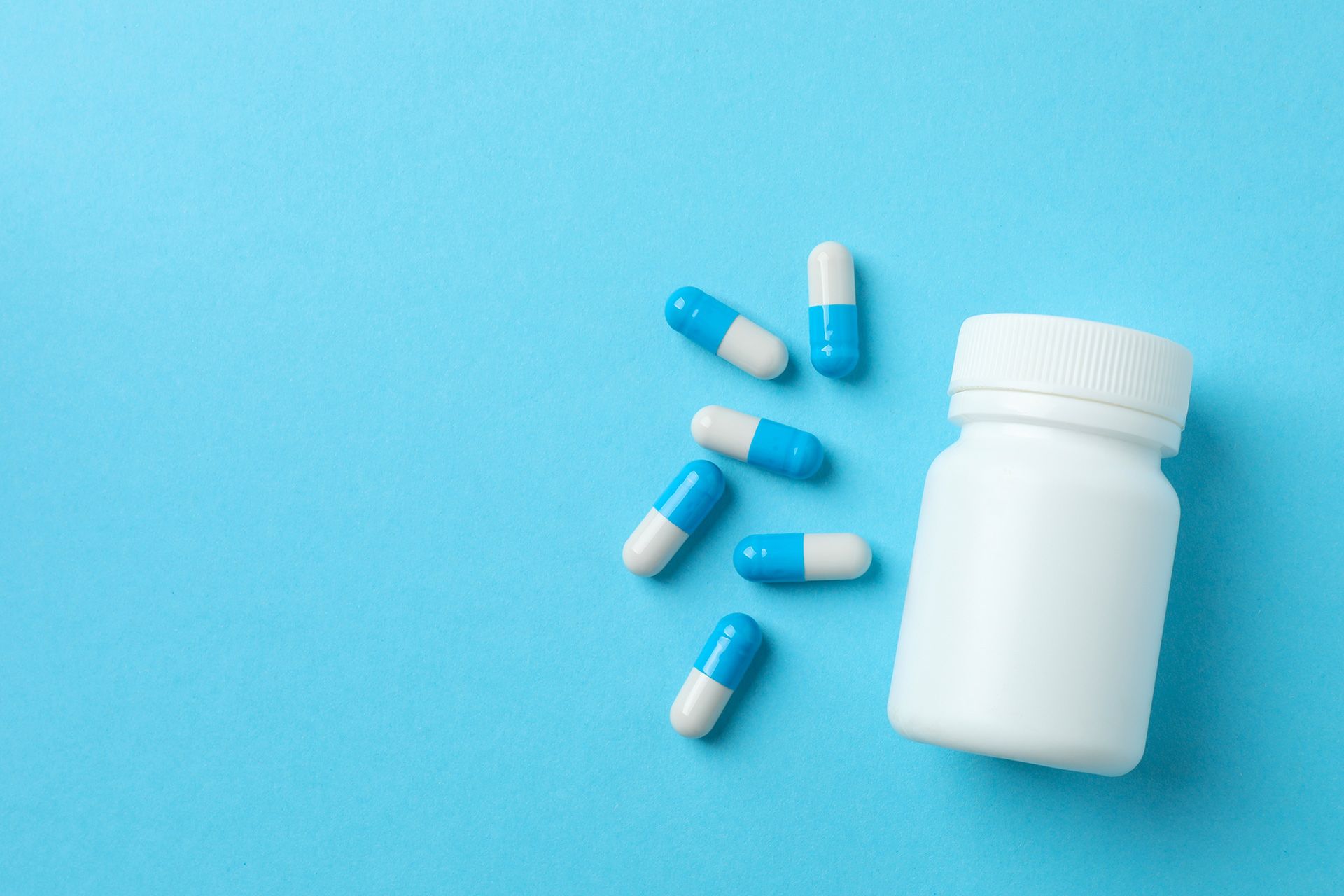 White pill bottle with blue-and-white capsules scattered on a blue background