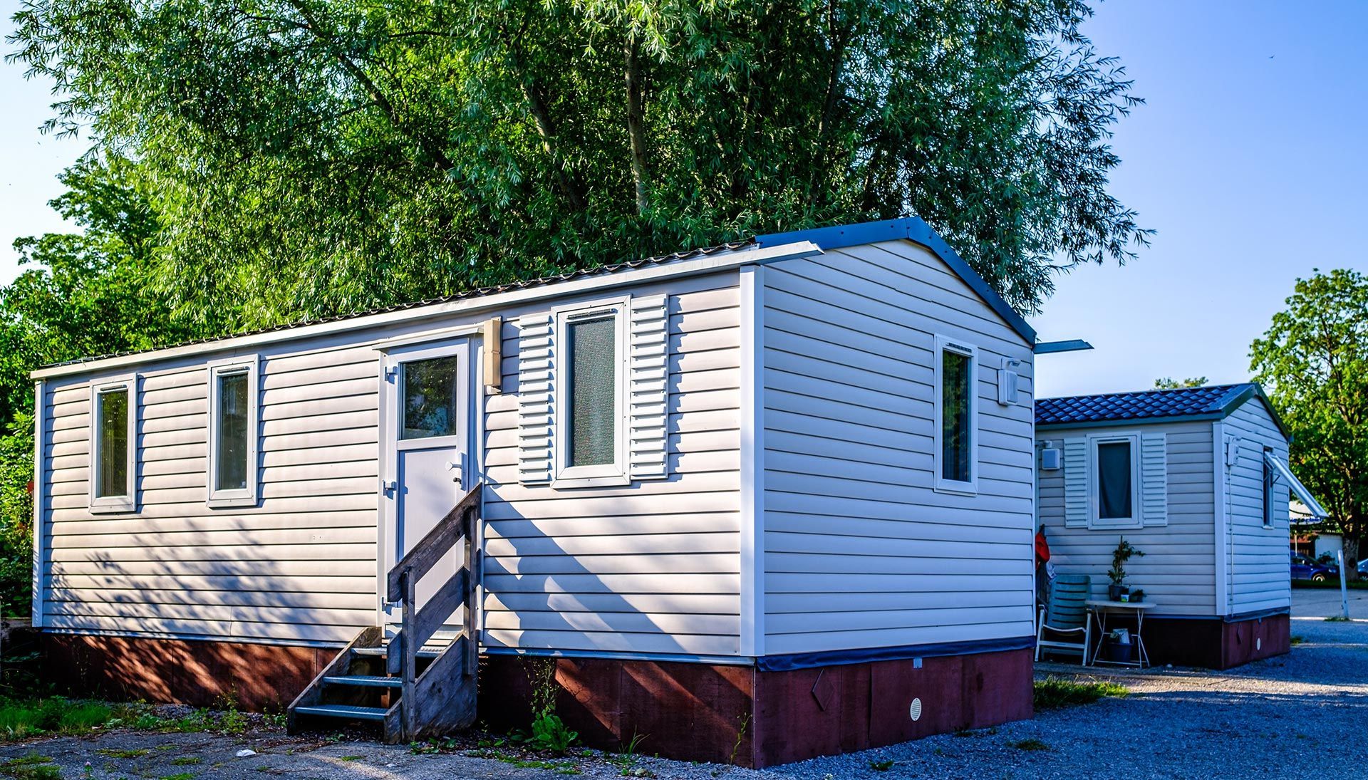 White mobile homes with blue trim in a sunny wooded lot
