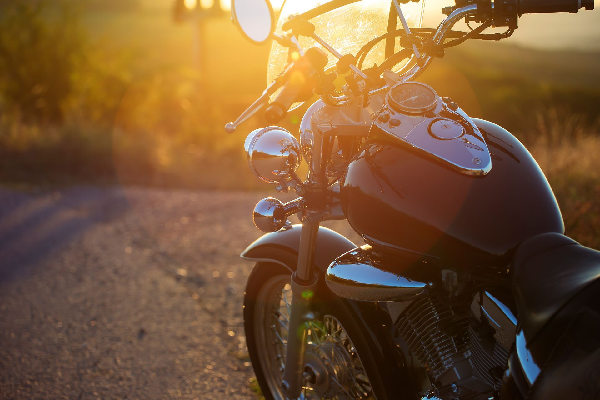 Motorcycle parked on a sunlit road at sunset, with warm golden light reflecting off the chrome.