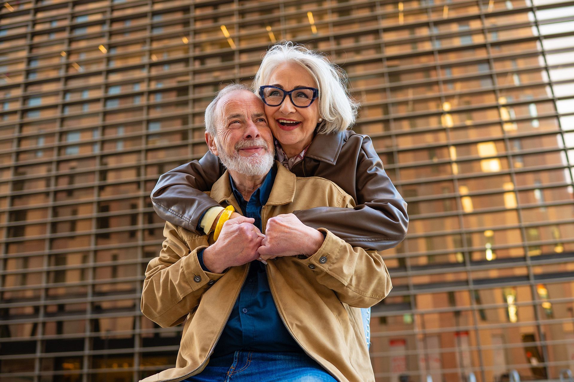 Smiling couple hugging in front of a modern glass building