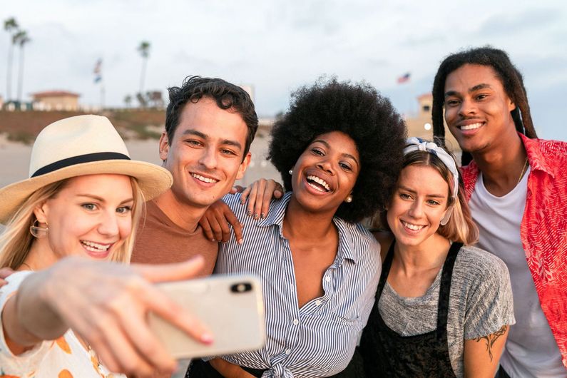 Five friends smiling and taking a selfie outdoors at sunset