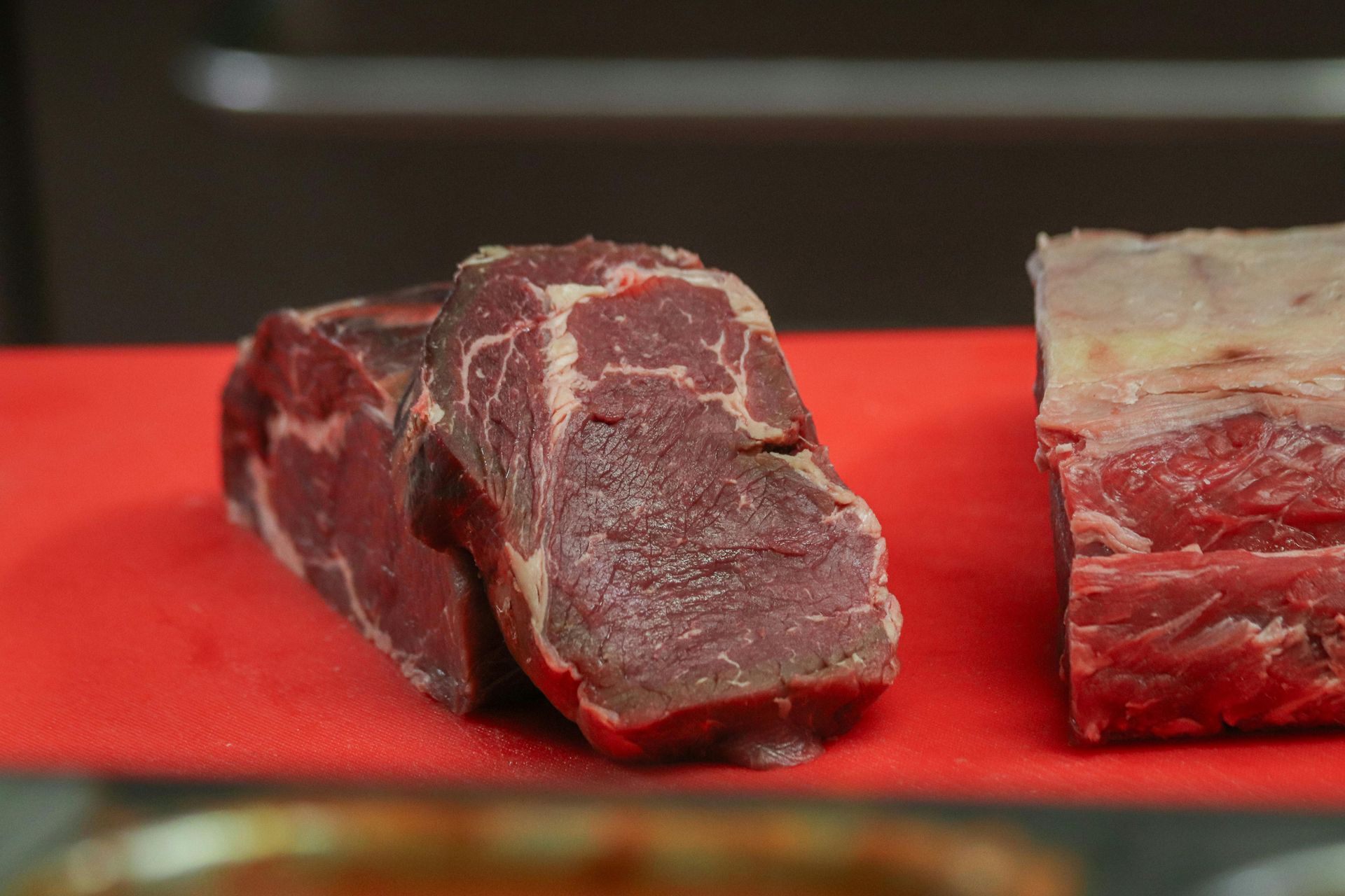 Eleven raw, marbled beef steaks arranged in rows on a black slate surface.