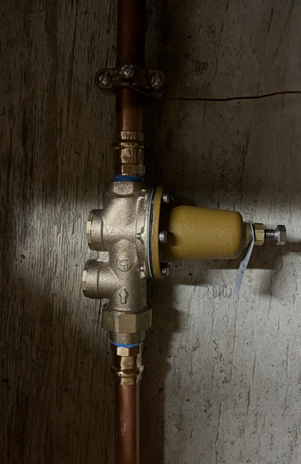 Old water valve assembly with copper pipes and a yellow filter on a concrete wall