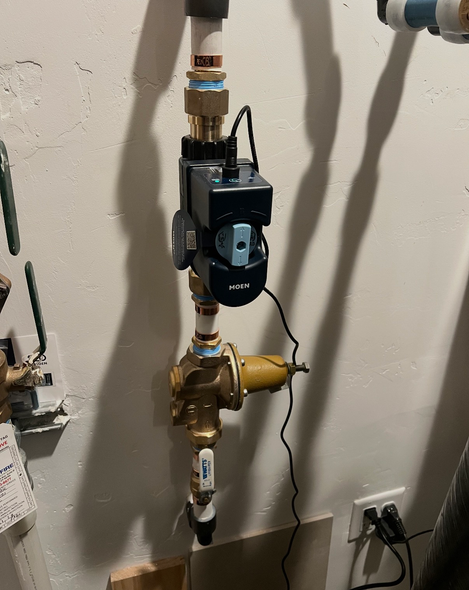 Wall-mounted water pump and brass plumbing valves beside an electrical outlet in a utility room