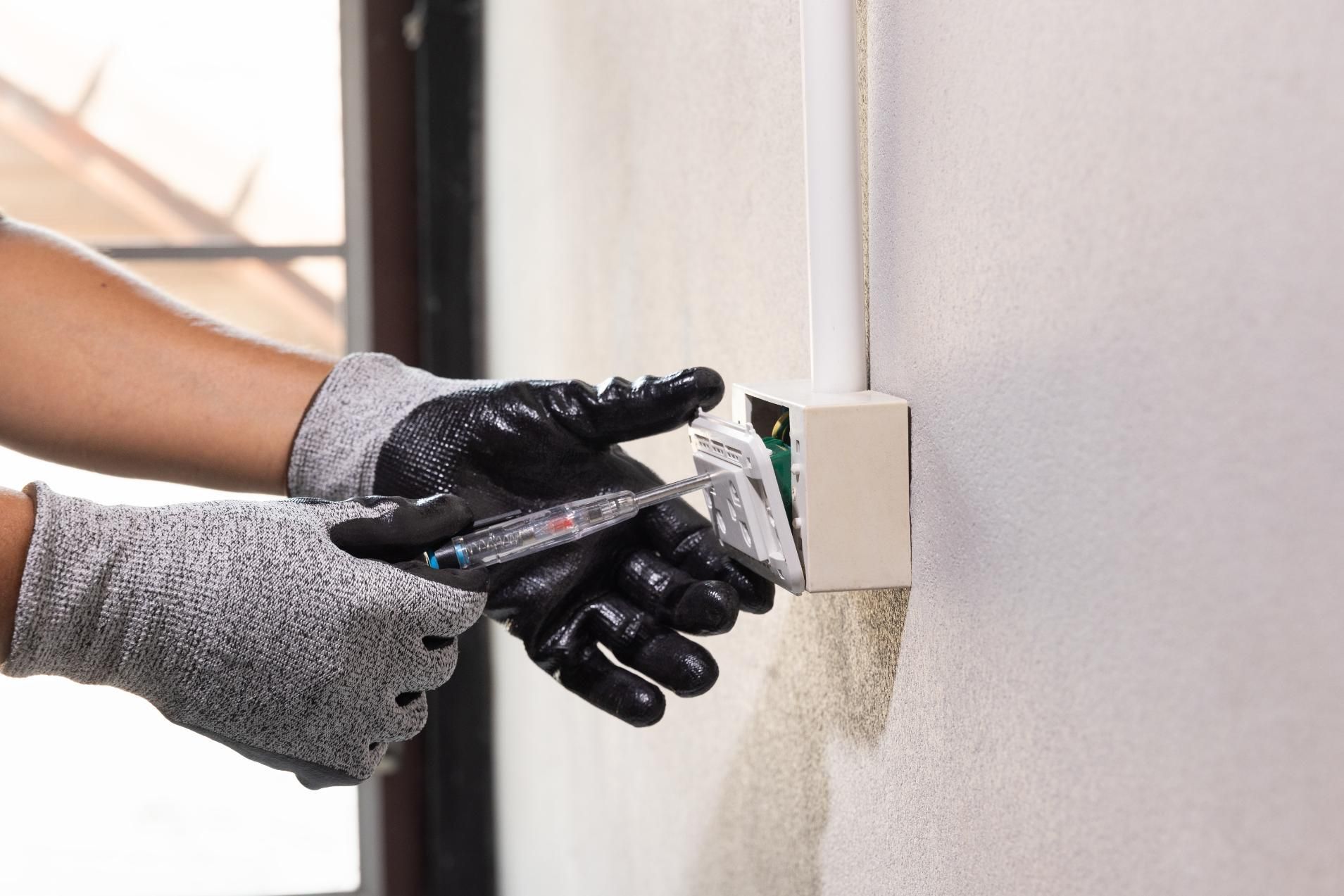 A person wearing gloves is plugging an outlet into a wall.
