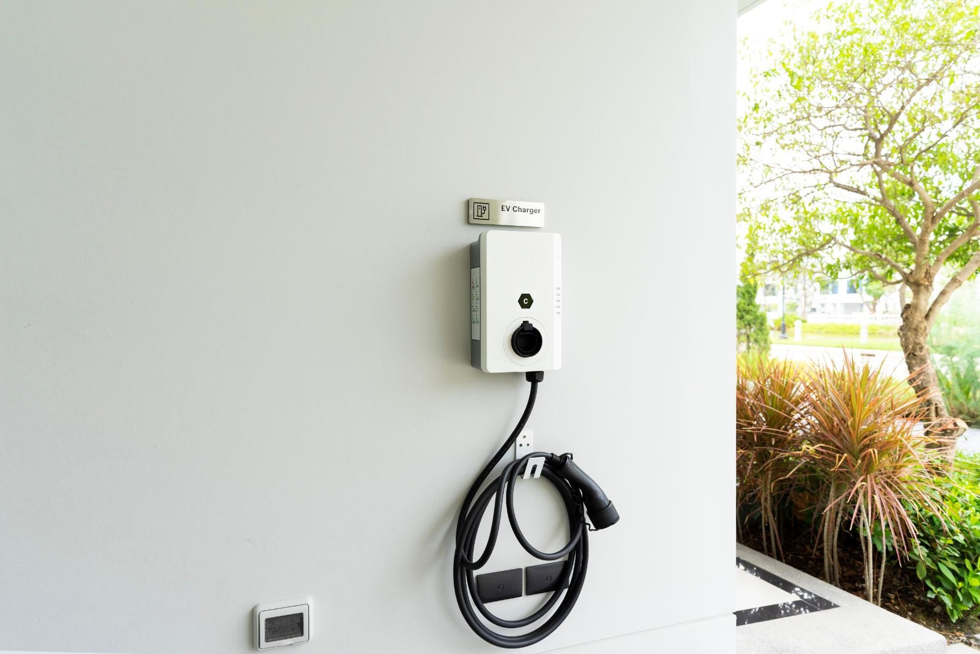 A white electric car charger is hanging on a white wall.