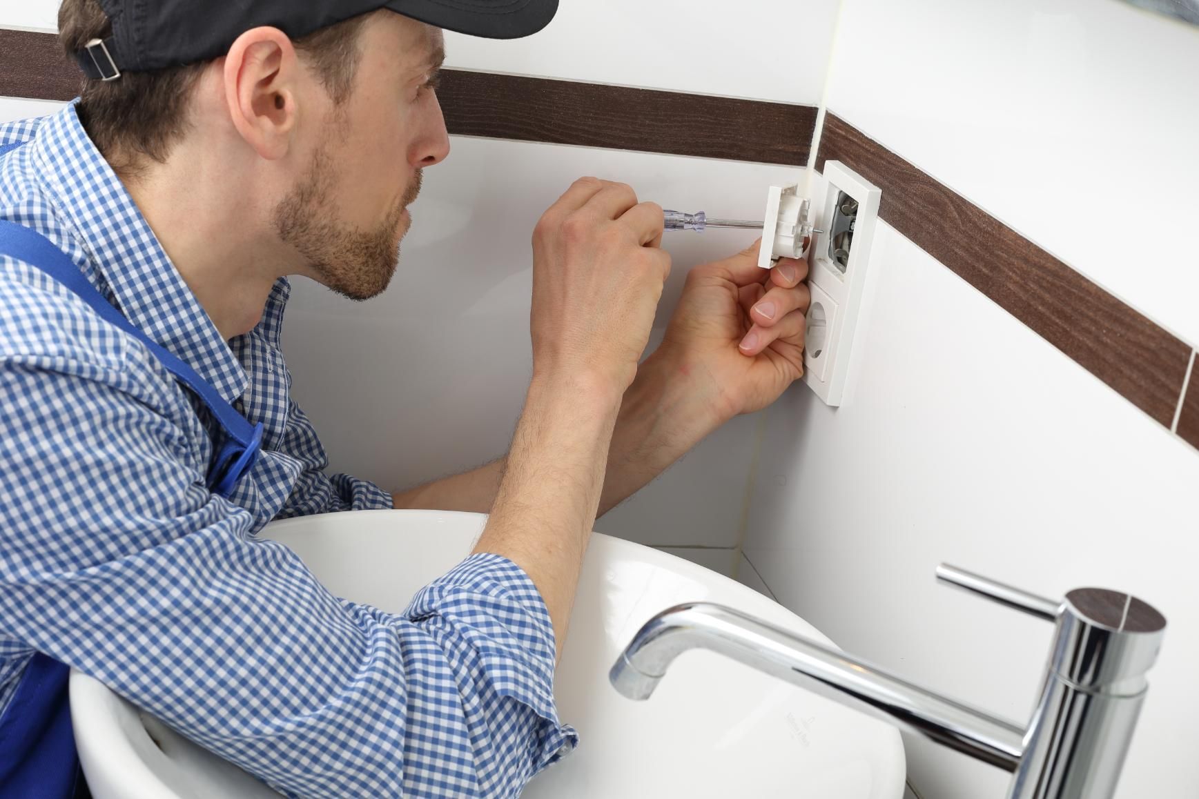 A man is working on a bathroom sink with a screwdriver.