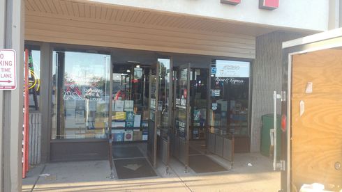 Storefront with glass doors, greeting cards and merchandise visible inside. Brown awnings and beige facade.