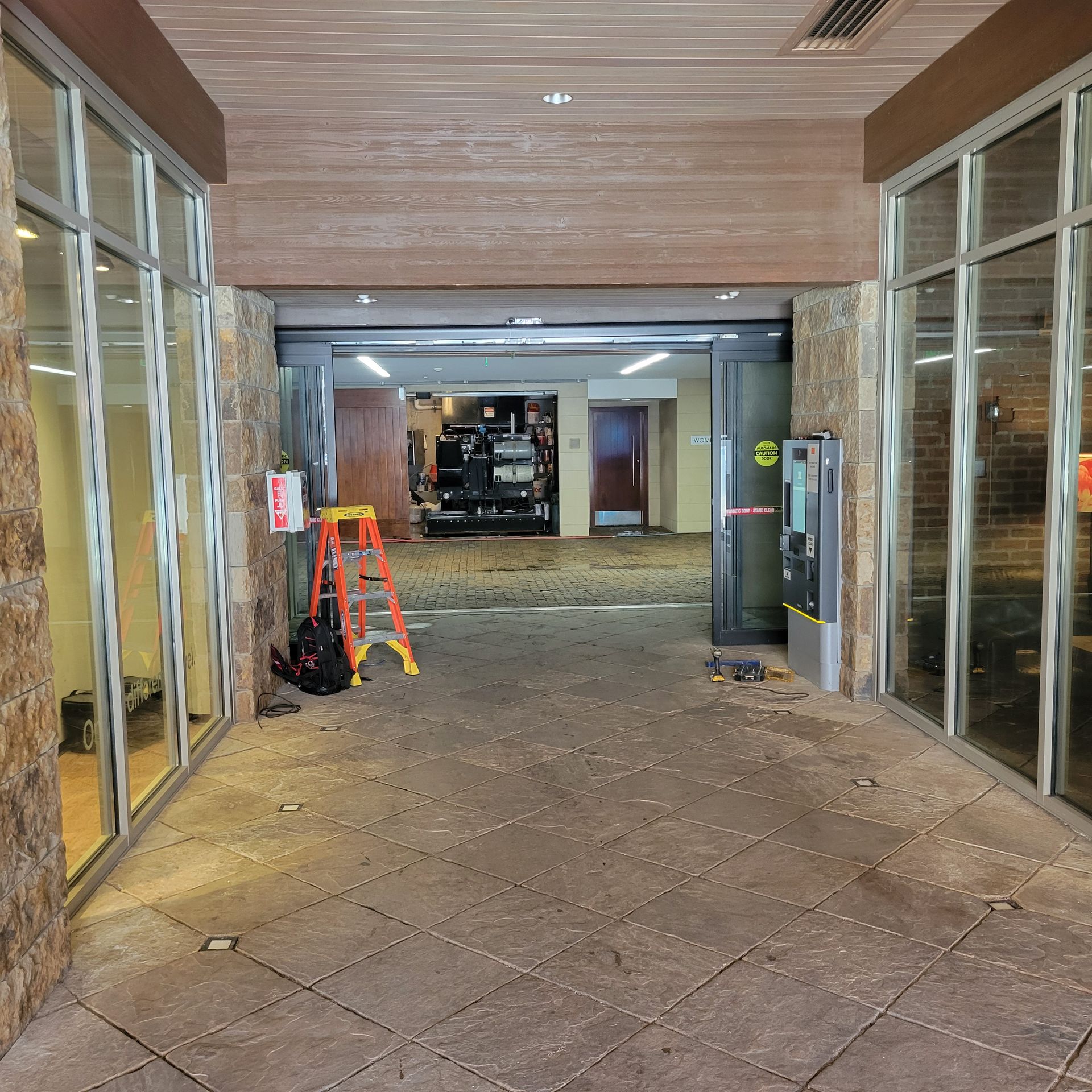 Entrance with glass windows, textured walls, and open door to interior with construction materials and equipment.