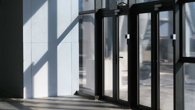 Sunlight on a white wall and glass doors, casting shadows.