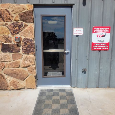 Doorway with stone wall and metal siding. A doormat leads to a blue door with a window. Signage on the right.