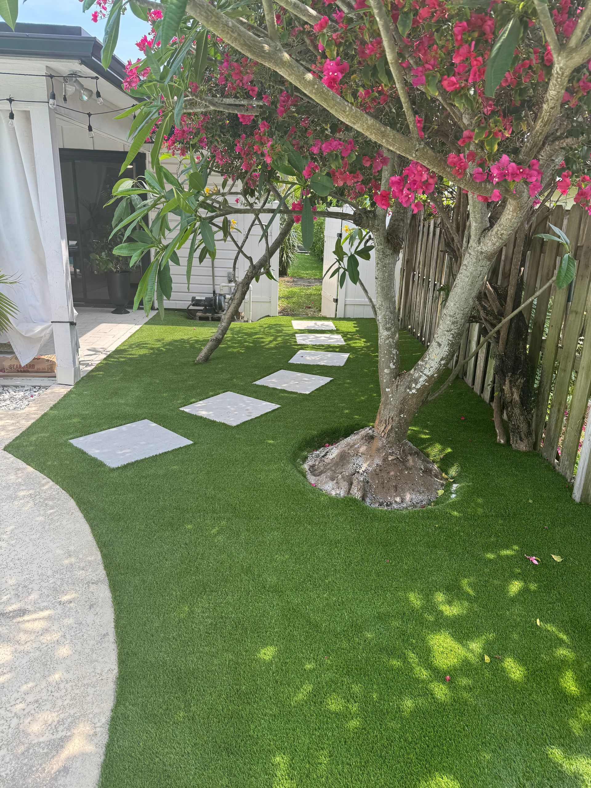 A lush green lawn with a tree and stepping stones in front of a house.