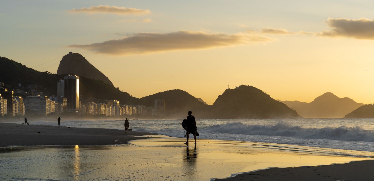 silhueta de um homem com uma prancha na mão em uma tarde na praia no rio de janeiro